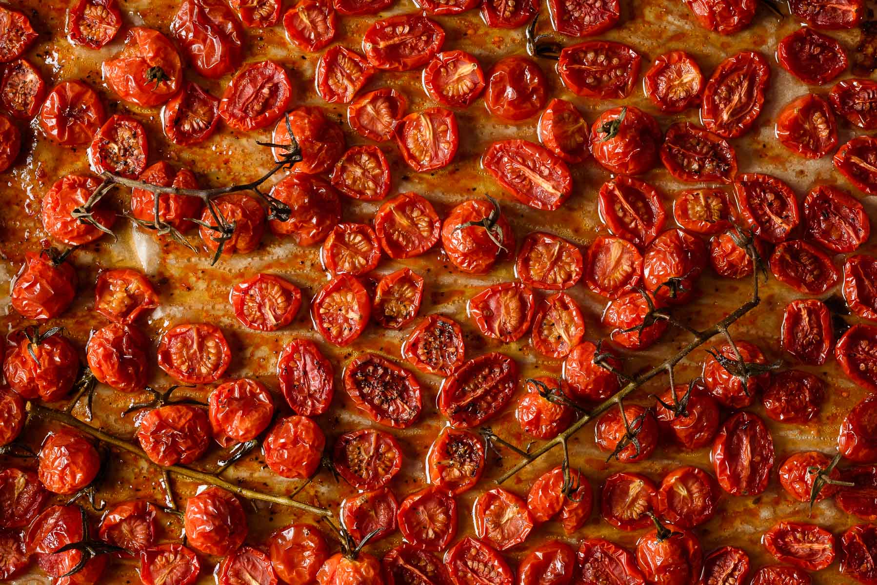 Roasted tomatoes in olive oil on a sheet pan.