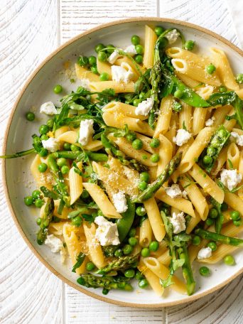 A plate of spring vegetable pasta with asparagus, peas, arugula, goat cheese, parmesan, lemon, and fresh herbs
