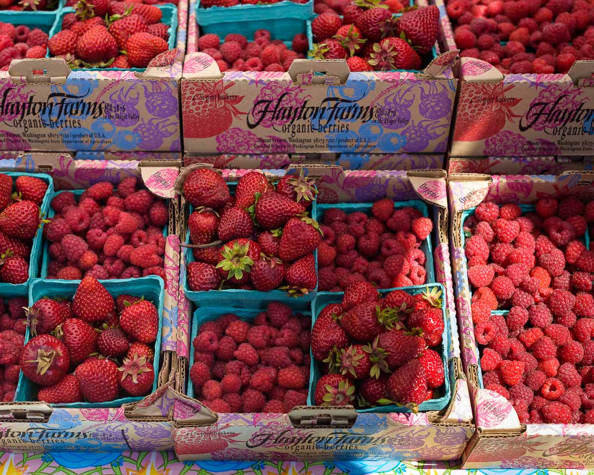 Boxes of fresh strawberries and raspberries stacked on a table at the farmers market.