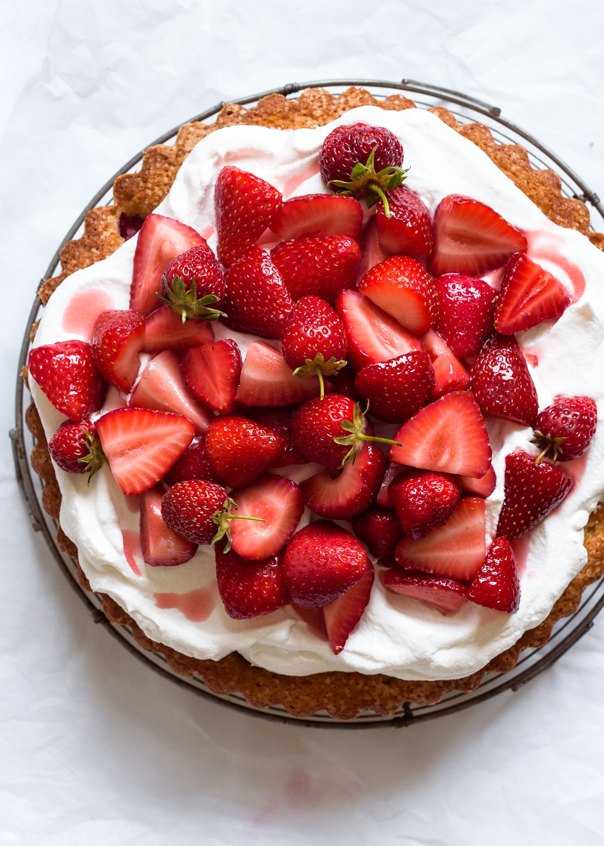 A strawberry almond buttermilk cake with whipped cream and macerated strawberries on a white background.