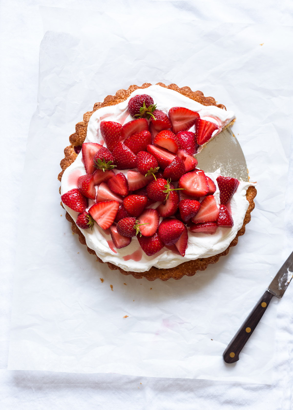 A strawberry almond buttermilk cake with whipped cream and macerated strawberries on a white background.