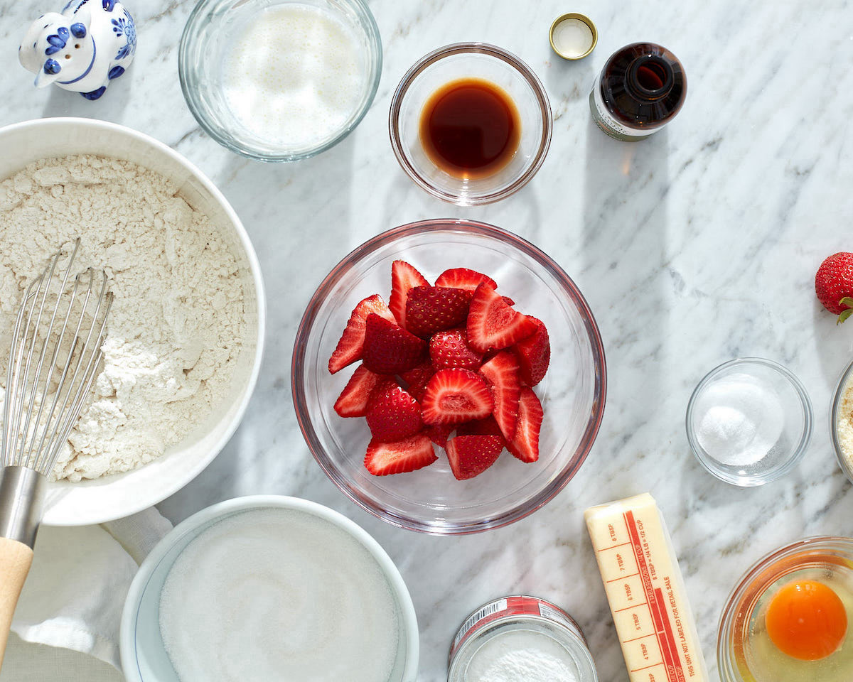 The ingredients to make a strawberry buttermilk cake in small bowls on a white marble counter.