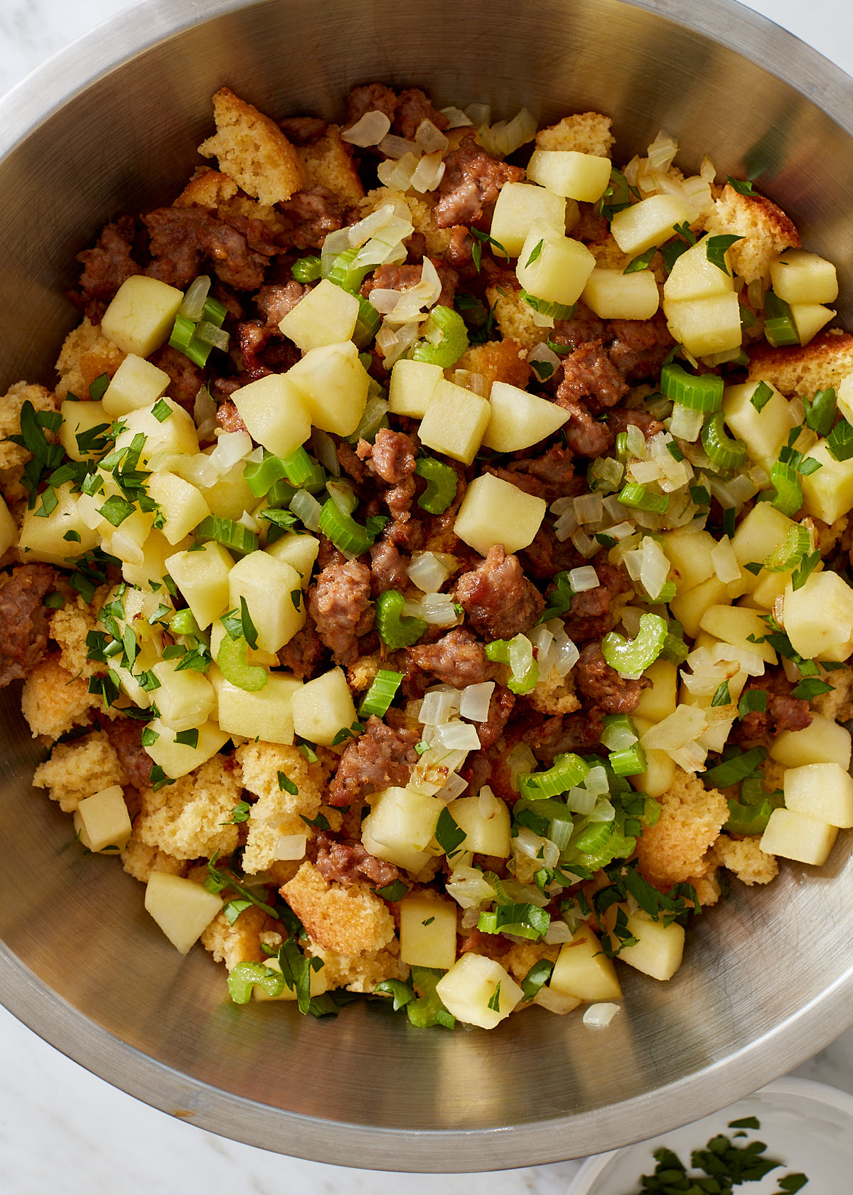 Close up of cornbread dressing ingredients (with sweet italian sausage, apple, onion, celery, and herbs), ready to be mixed before baking.