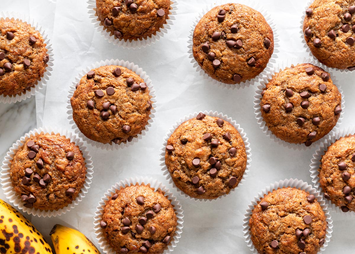 A batch of chocolate chip banana muffins on a white parchment paper background.