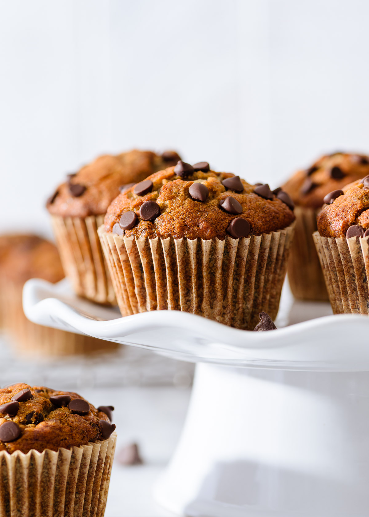 Chocolate chip banana muffins on a white cake stand with a light background.