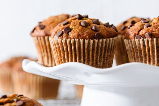 Chocolate chip banana muffins on a white cake stand with a light background.