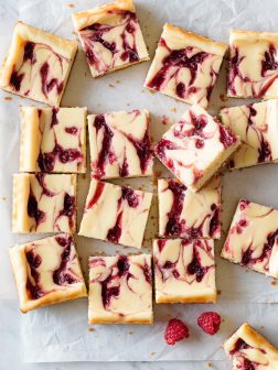 raspberry swirled white chocolate cheesecake bar squares on a parchment paper and marble background.
