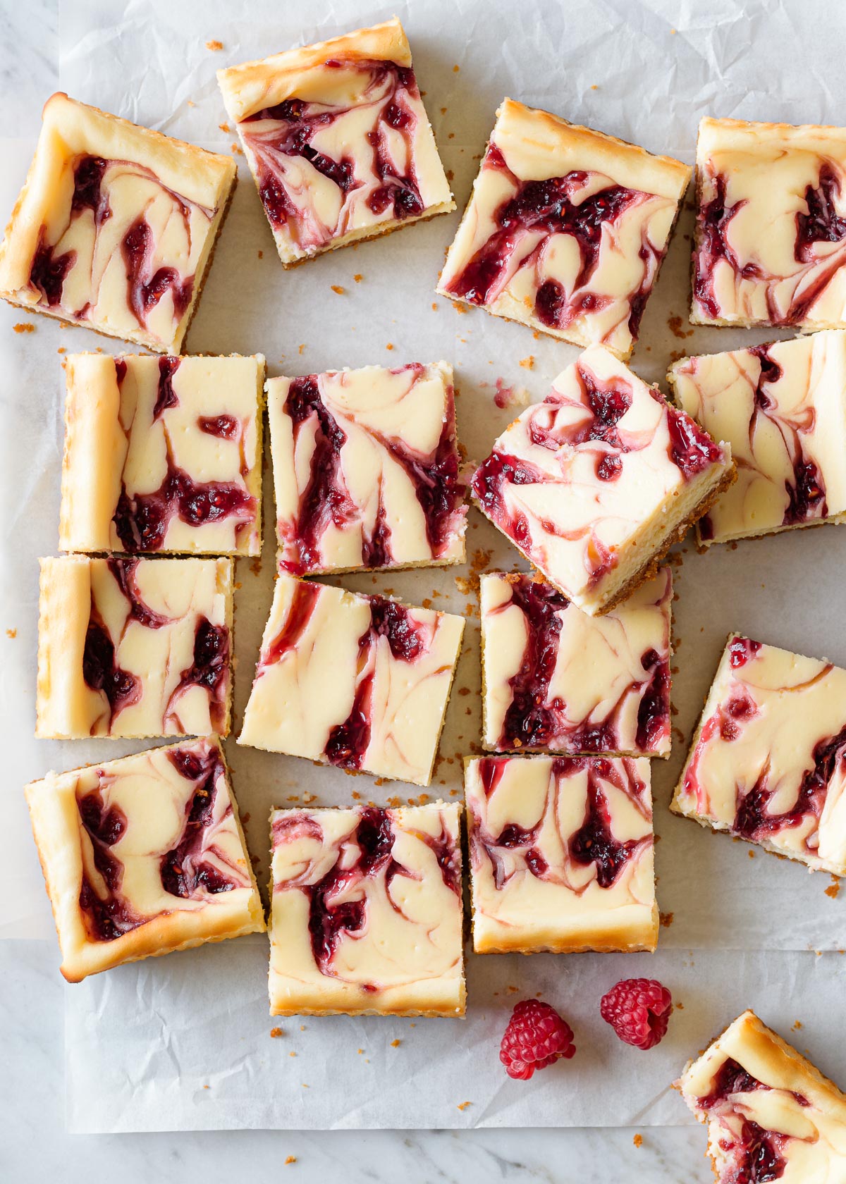 raspberry swirled white chocolate cheesecake bar squares on a parchment paper and marble background.