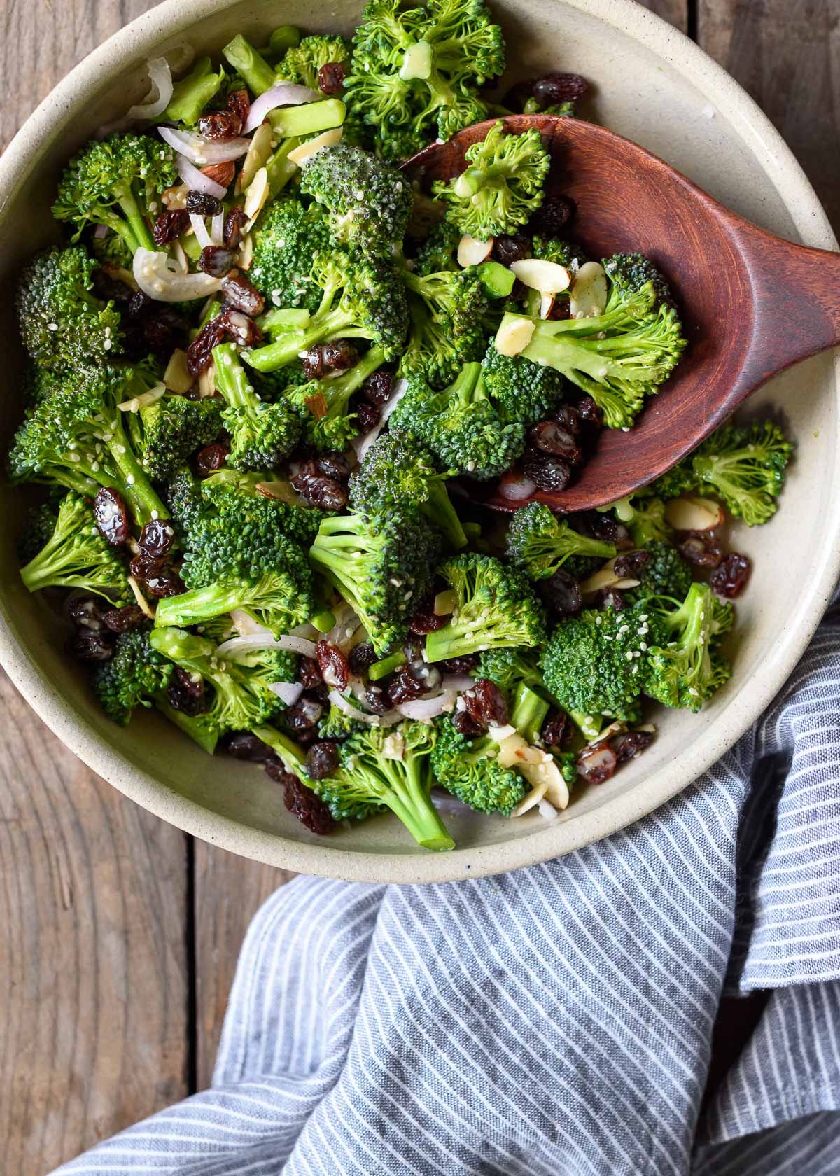 A bowl of broccoli salad with shallots, almonds, raisins, and a lemon tahini dressing.
