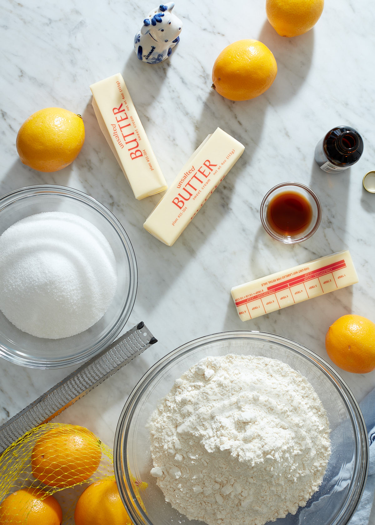 Baking ingredients to make lemon shortbread squares on a marble background. Butter, flour, sugar, lemon, salt, and vanilla.