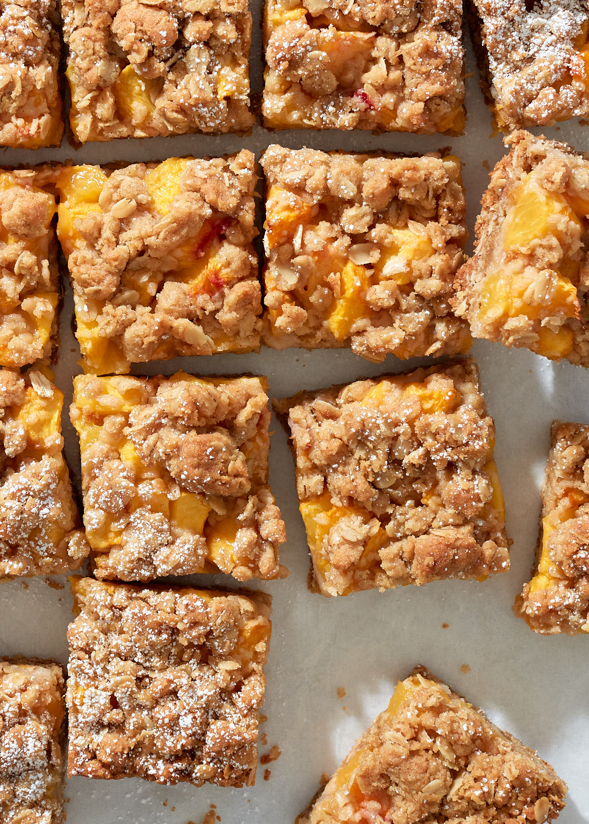 close up of sliced peach crumble bars dusted with powdered sugar.