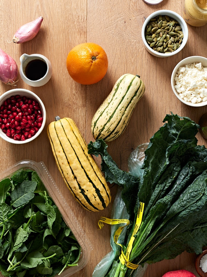 The ingredients to make a Fall delicata squash salad on a light wood table.