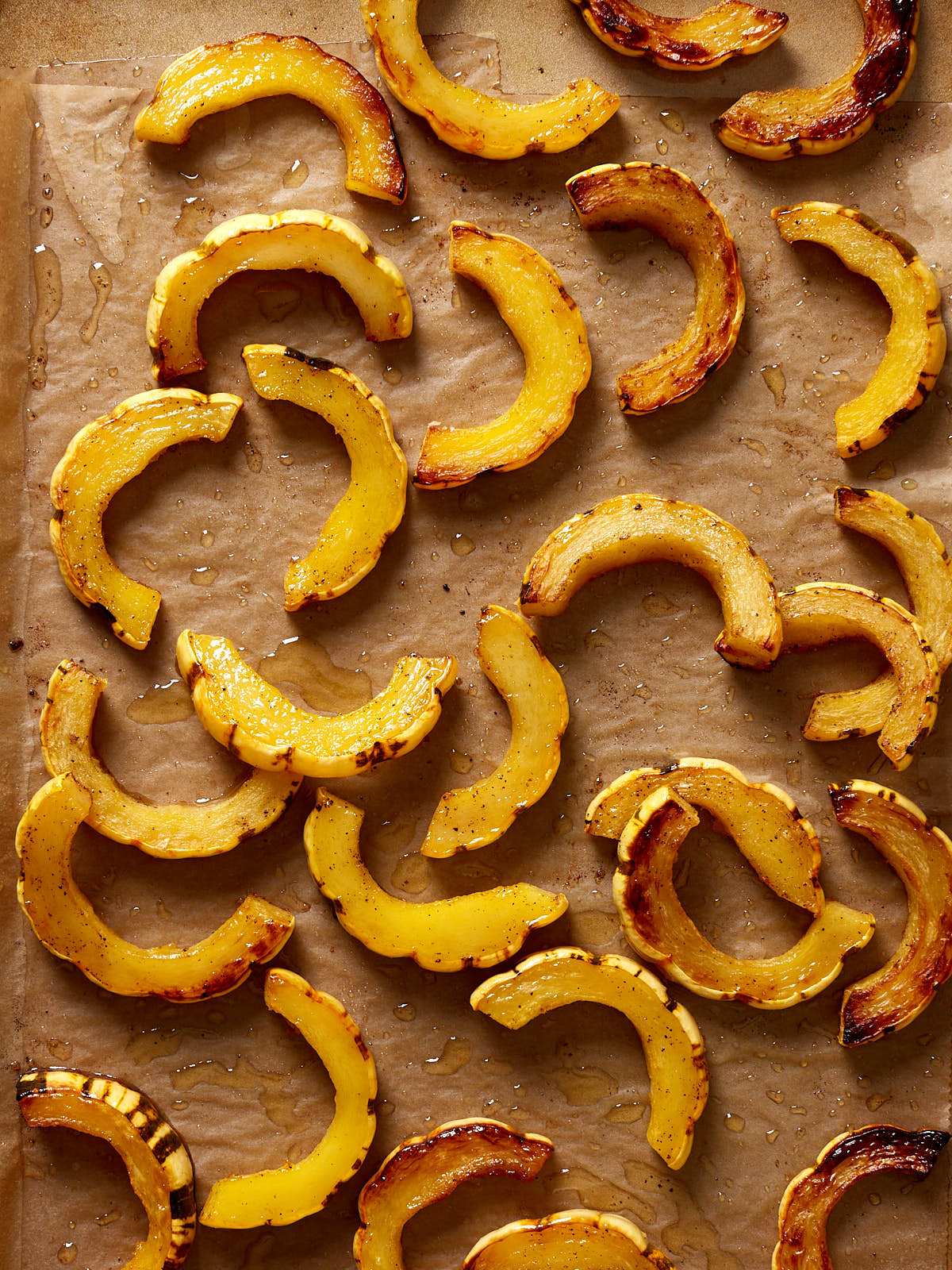 Slices of roasted delicata squash on a natural parchment paper lined baking sheet.