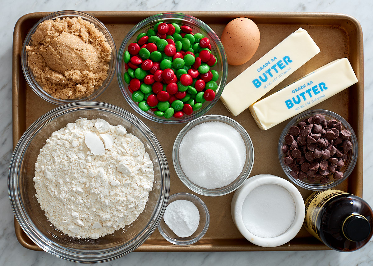 The ingredients to make holiday M&M cookie bars prepped on a baking sheet on a marble counter.
