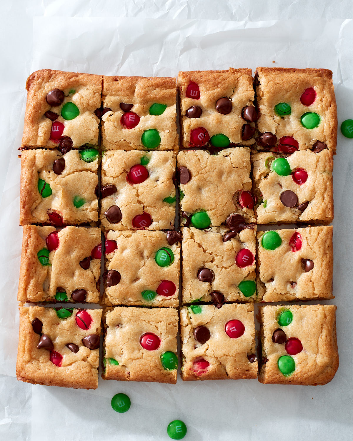 Sliced M&M cookie bars on white parchment paper on a marble counter top.