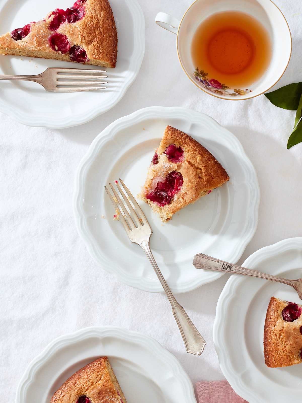 Citrus and Cranberry Buttermilk Cake | Slices of cranberry cake on white porcelain dessert plates with vintage forks, pink linen, tea, and fresh tangerines.