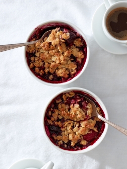 Two miniature mixed berry crumbles on a white linen background with little cups of espresso.
