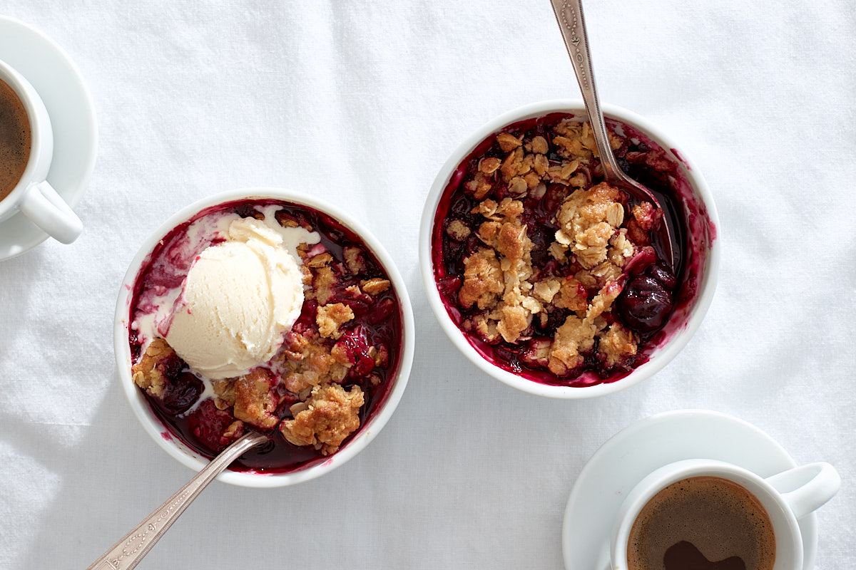 Two individual mixed berry crumbles, with ice cream on top.