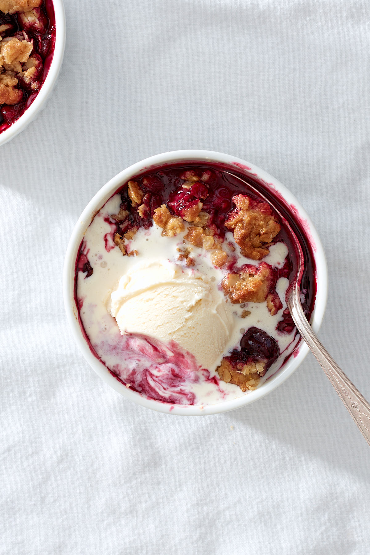 A close up of an individual mixed berry crumble with vanilla ice cream.