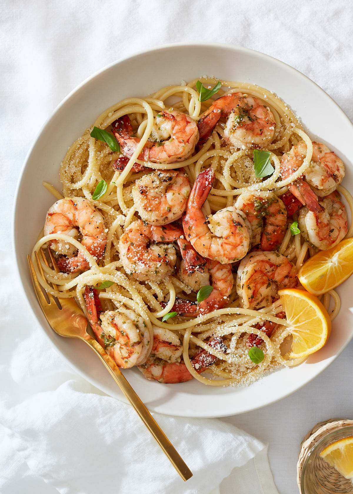 A bowl of shrimp pasta with garlic, lemon, and herbs on a white linen background.