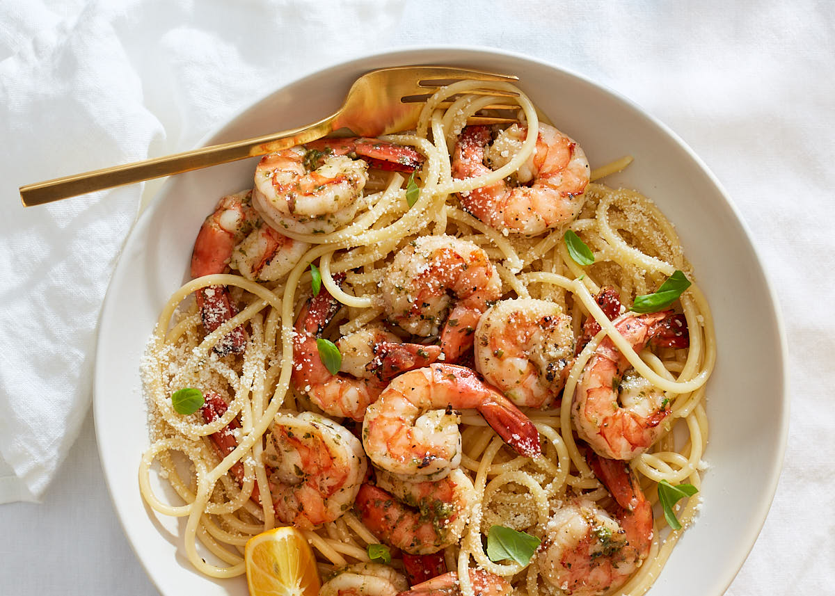 A bowl of lemon shrimp pasta with garlic, lemon, and herbs on a white linen background.