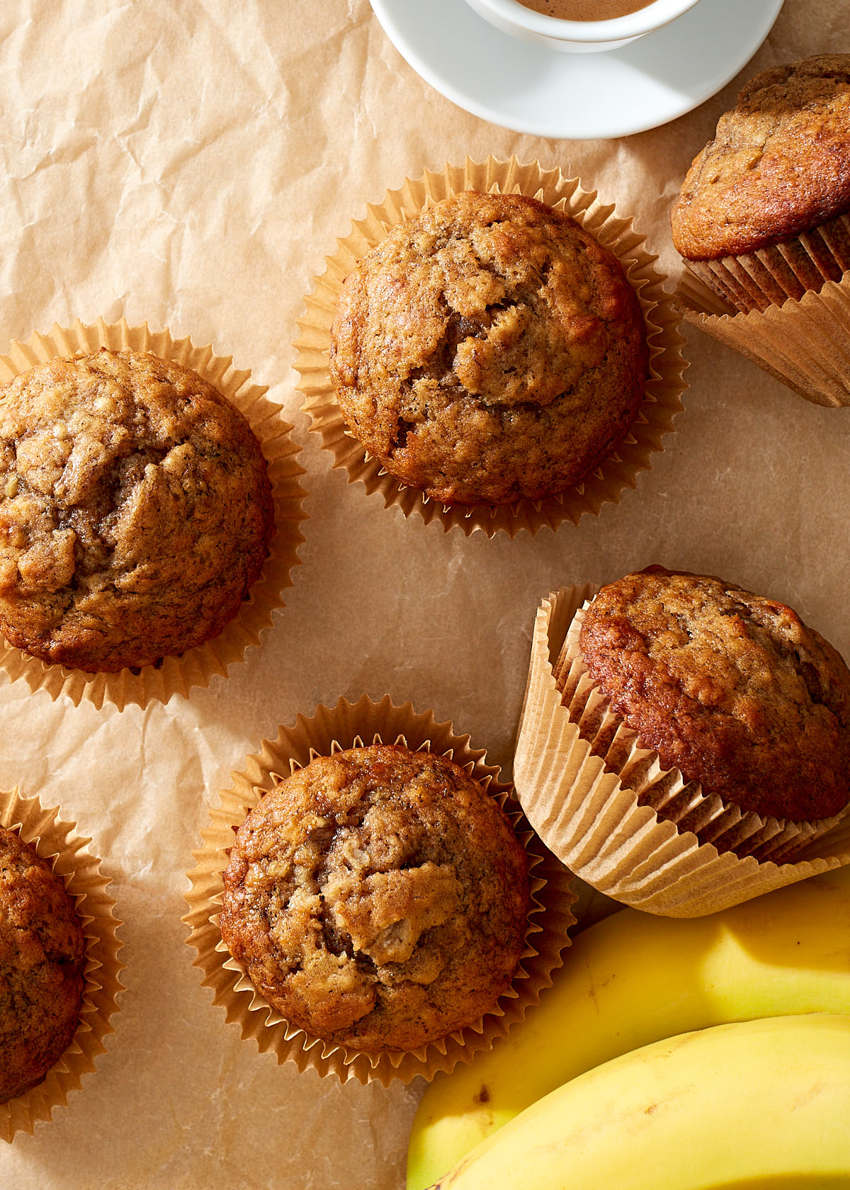 Simple banana muffins on natural parchment paper with a cup of espresso and a bunch of yellow bananas.