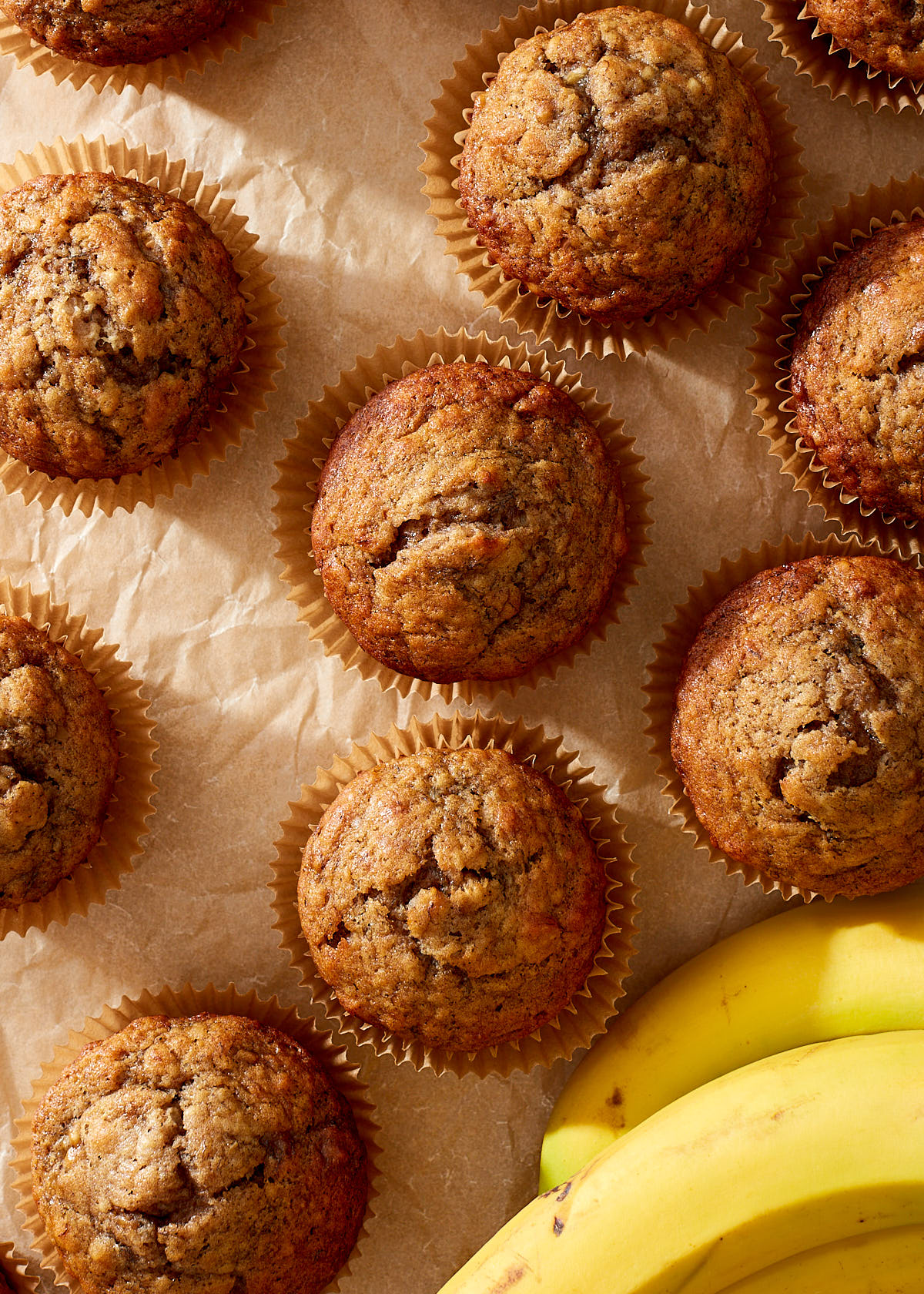 Simple banana muffins on natural parchment paper with a few yellow bananas.