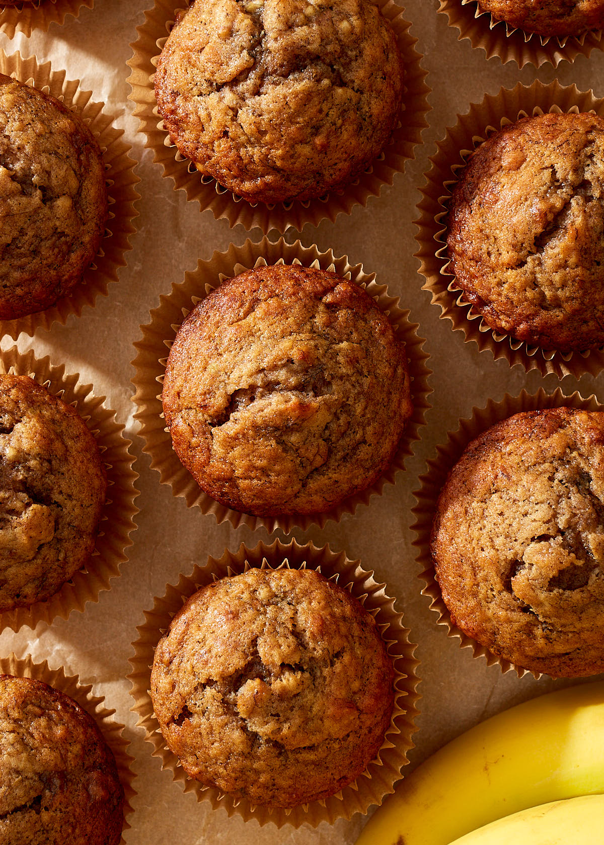 Simple banana muffins on natural parchment paper with a few yellow bananas.