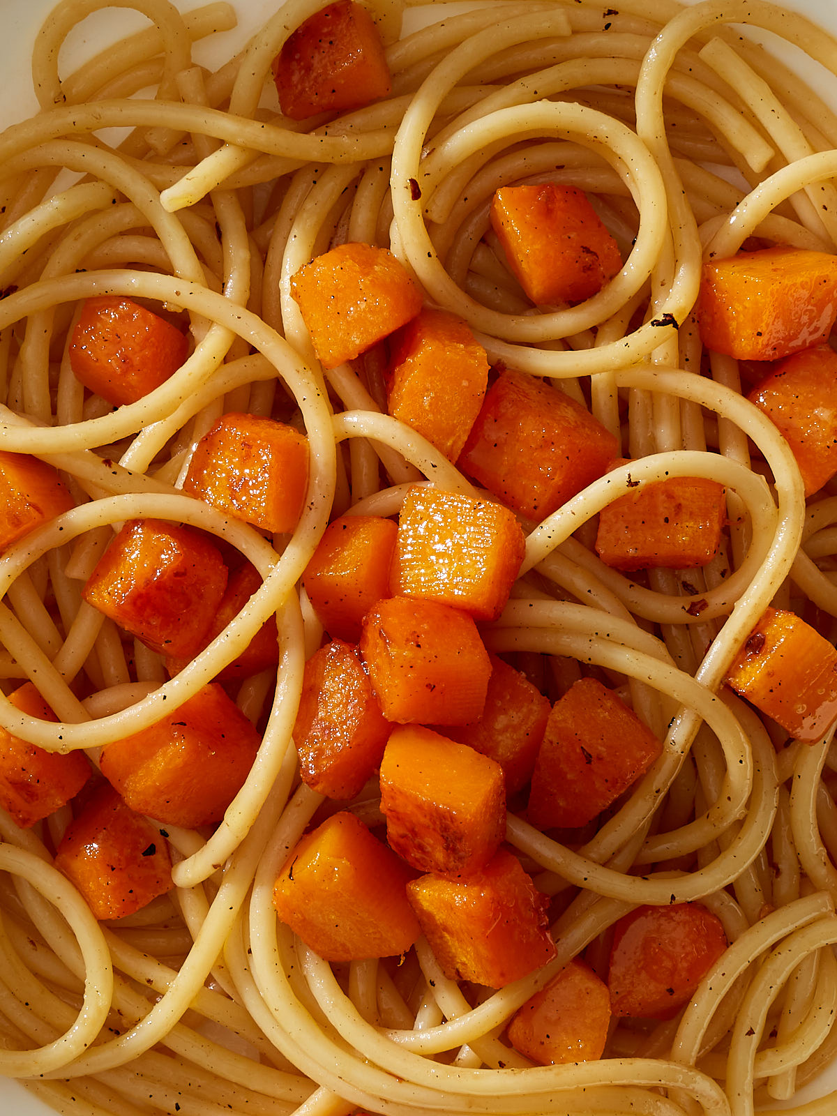 A close up of bucatini pasta in a sage butter sauce topped with cubes of caramelized butternut squash.
