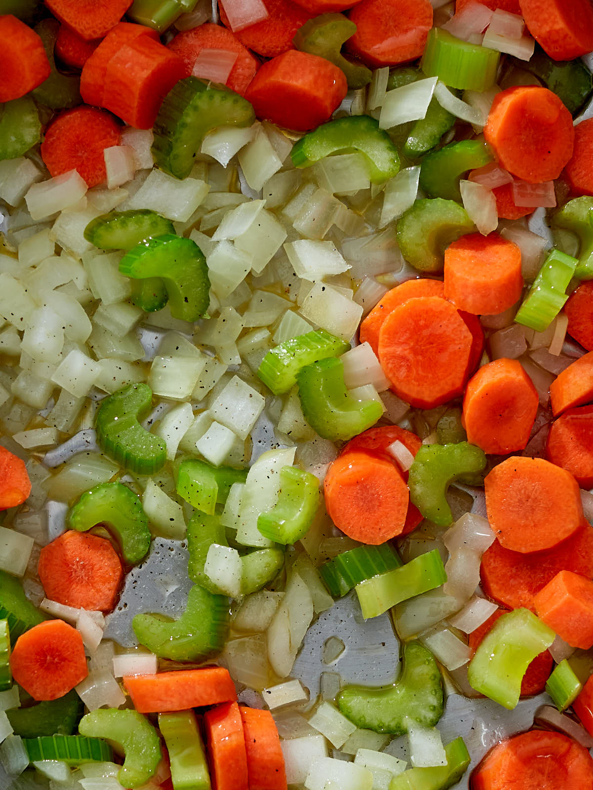Close up of the beginnings of a mirepoix (onion, carrots, and celery) with olive oil in a pan.
