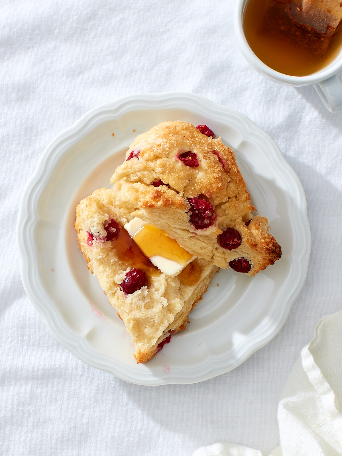 A cranberry scone, split open with butter and honey on a white dessert plate.