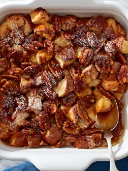 Homemade bread pudding with caramel and pecans in a white ceramic baking dish.