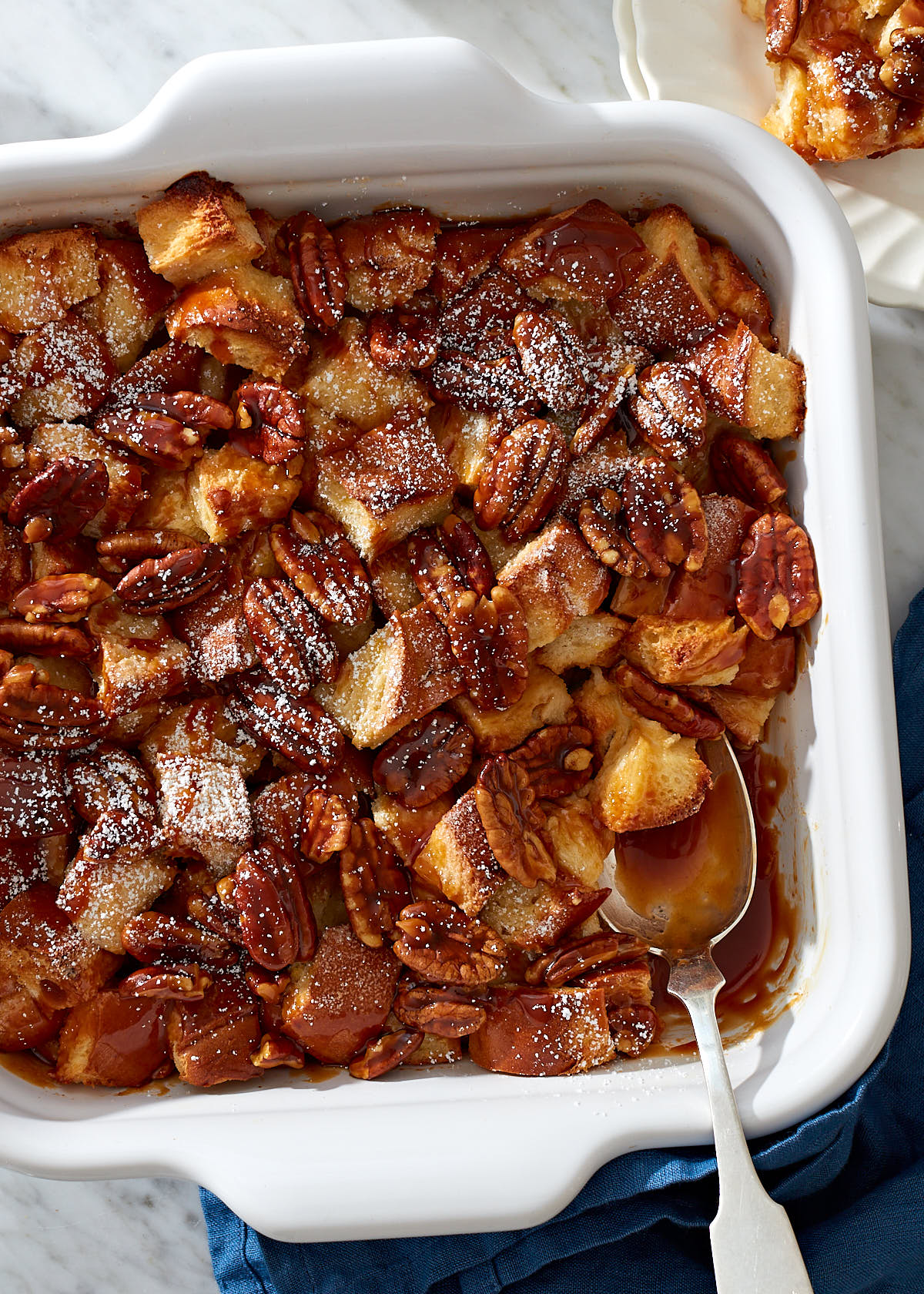 Homemade bread pudding with caramel and pecans in a white ceramic baking dish.