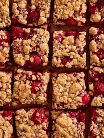 Rows of sliced raspberry and cranberry crumb bars on parchment paper.