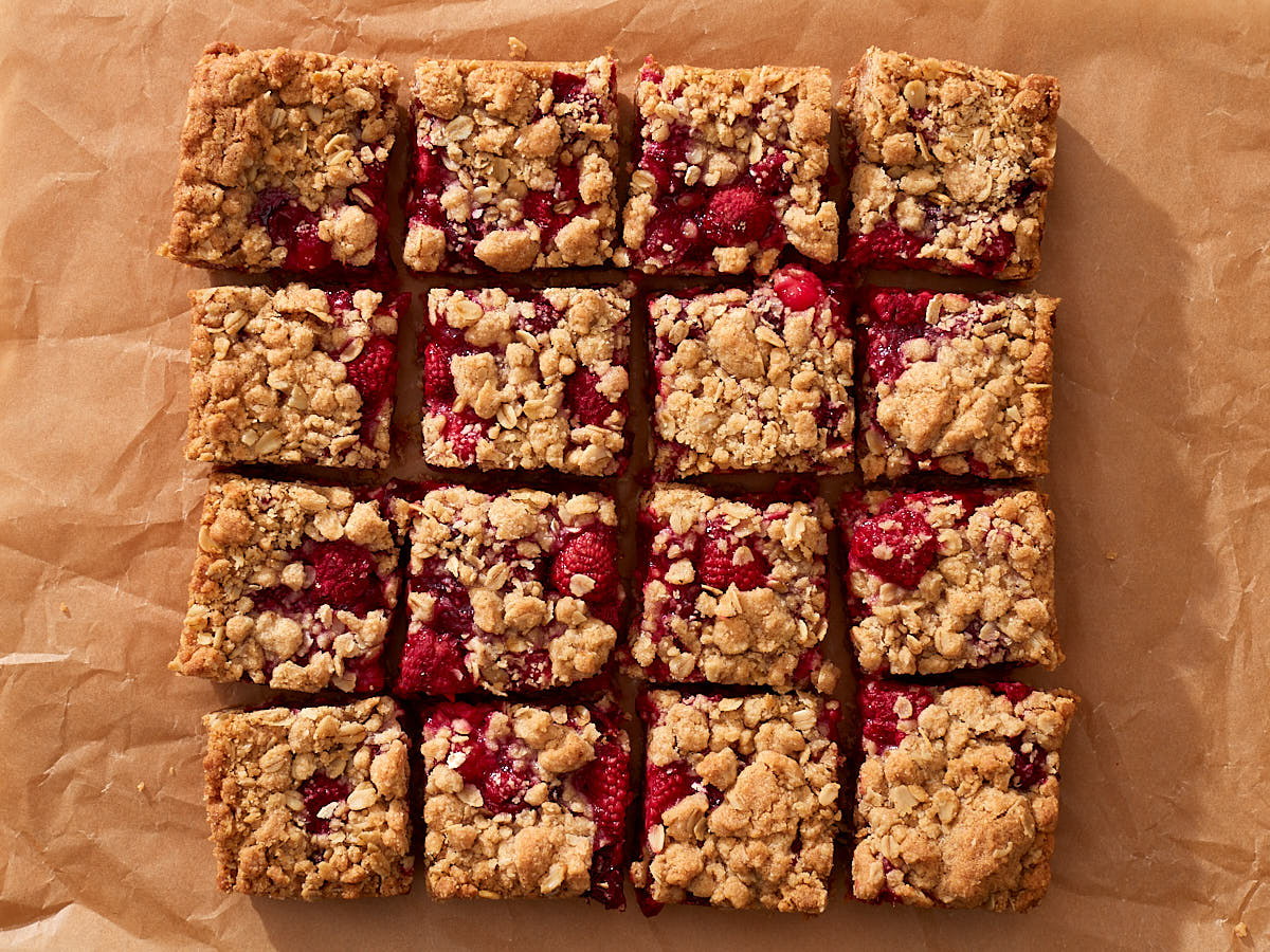 Rows of sliced raspberry and cranberry crumb bars on parchment paper.