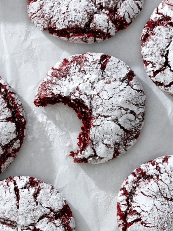 A red velvet crinkle cookie with a bite out of it on white parchment paper.